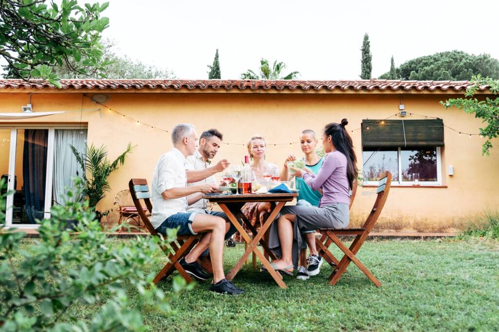 Longview of a group of a adult friends having a dinner party in the house backyard with beer and